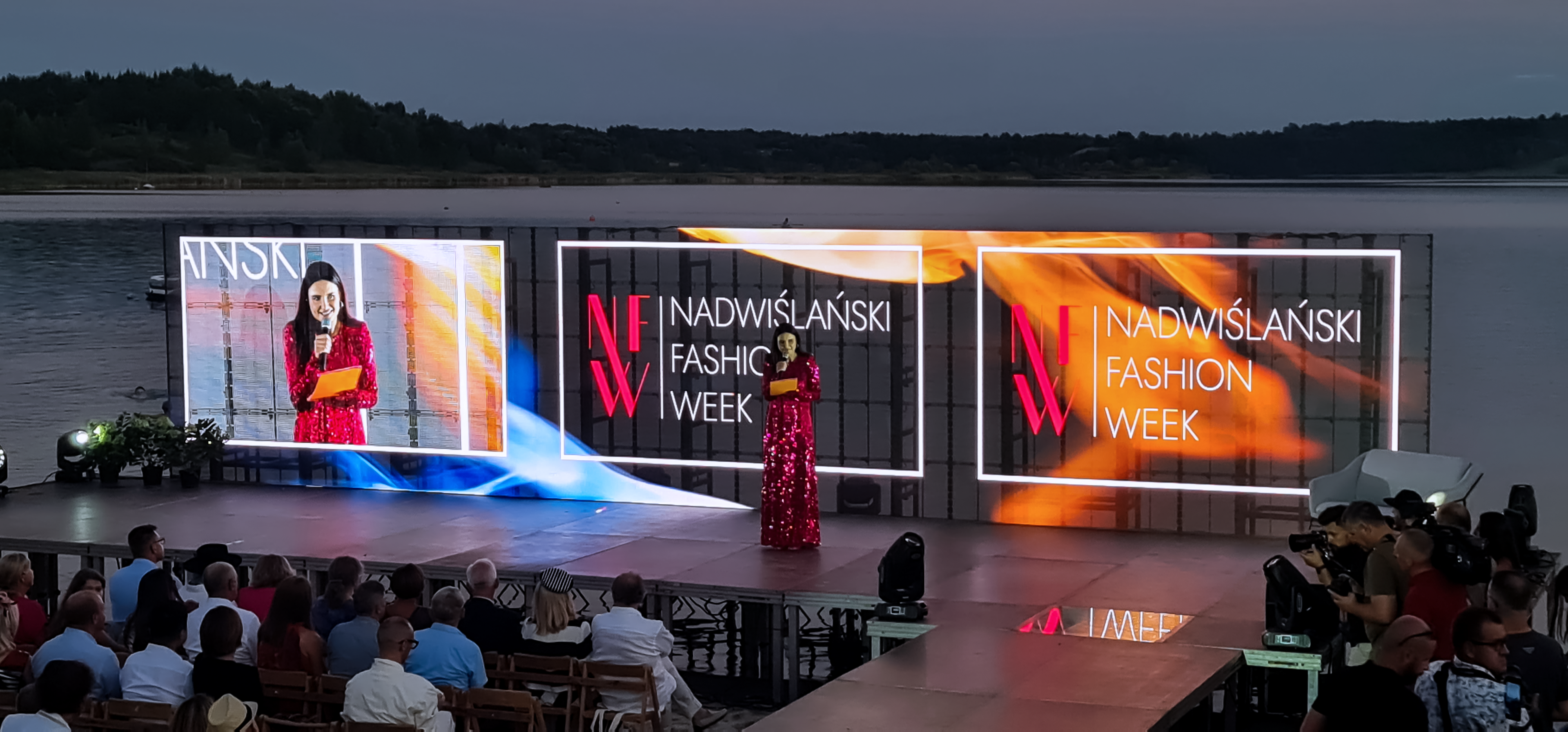 Joanna Horodyńska na scenie ustawionej na tafli jeziora Tarnobrzeskiego, a w tle transparentne ekrany LED reklamujące Nadwiślański Fashion Week