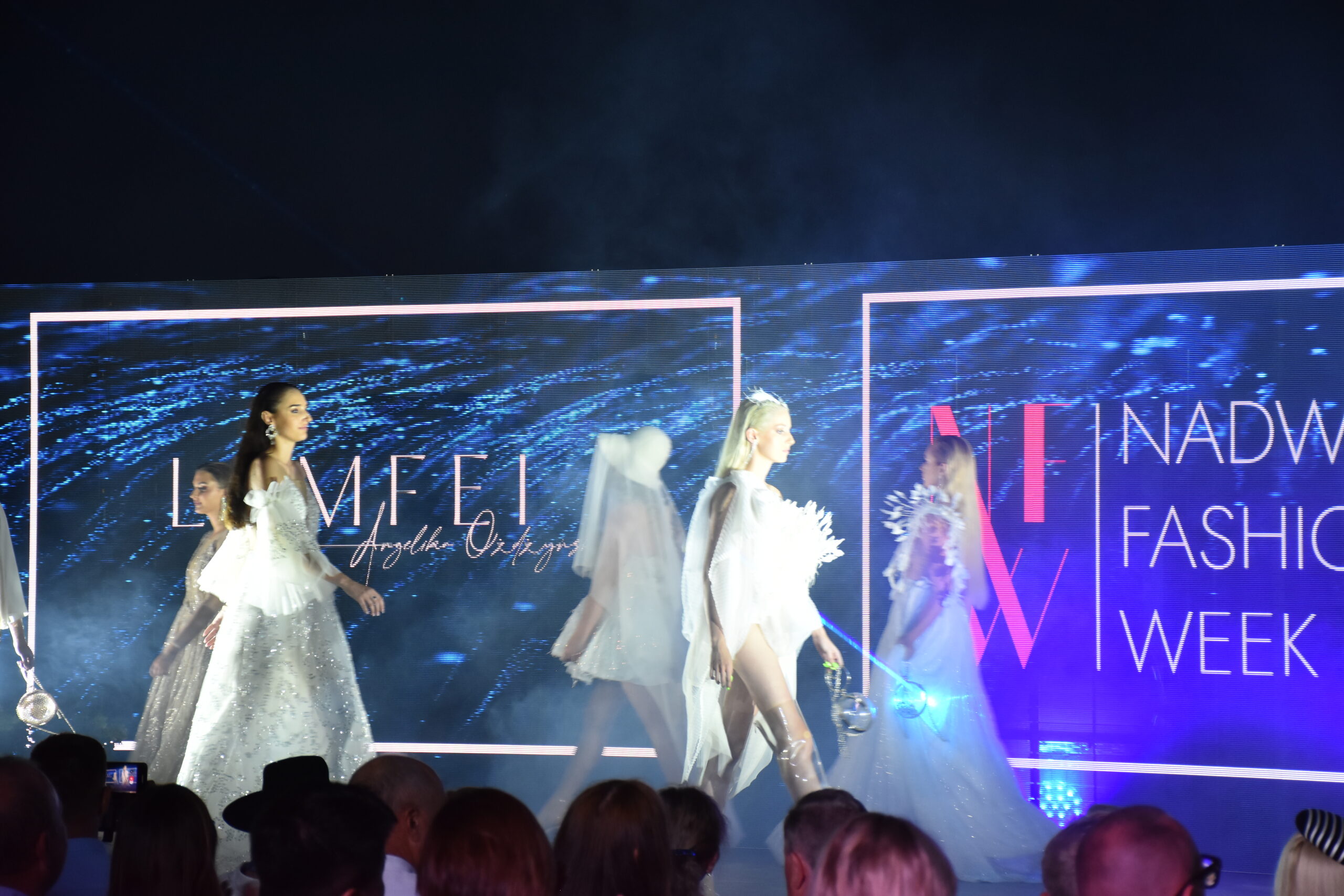 Modelki na wybiegu w trakcie Nadwiślańskiego Fashion Week - w tle transparentne ekrany LED z logo projektanta