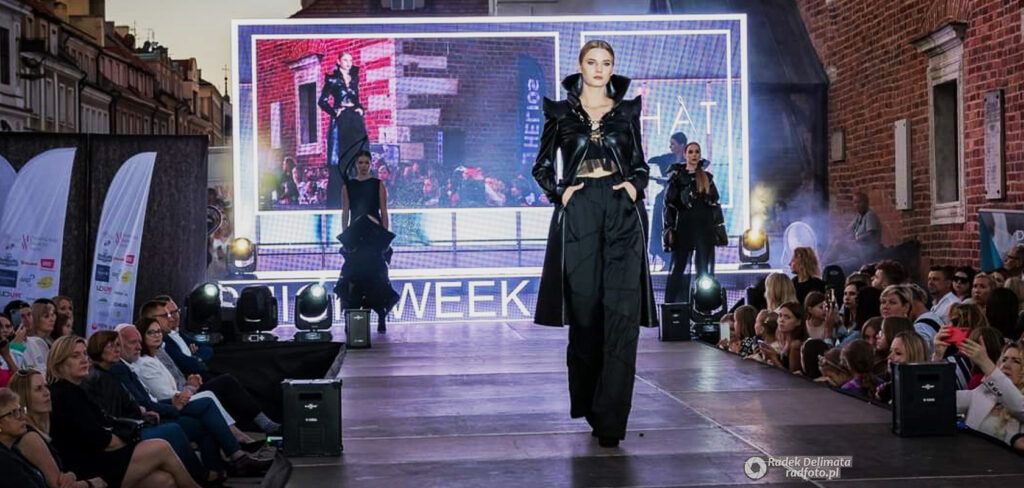 Modelka ubrana na czarno idąca po wybiegu na tle ekranu LED w trakcie Nadwiślanski Fashion Week